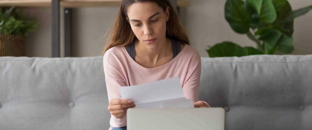 Upset woman sitting on couch at home near computer