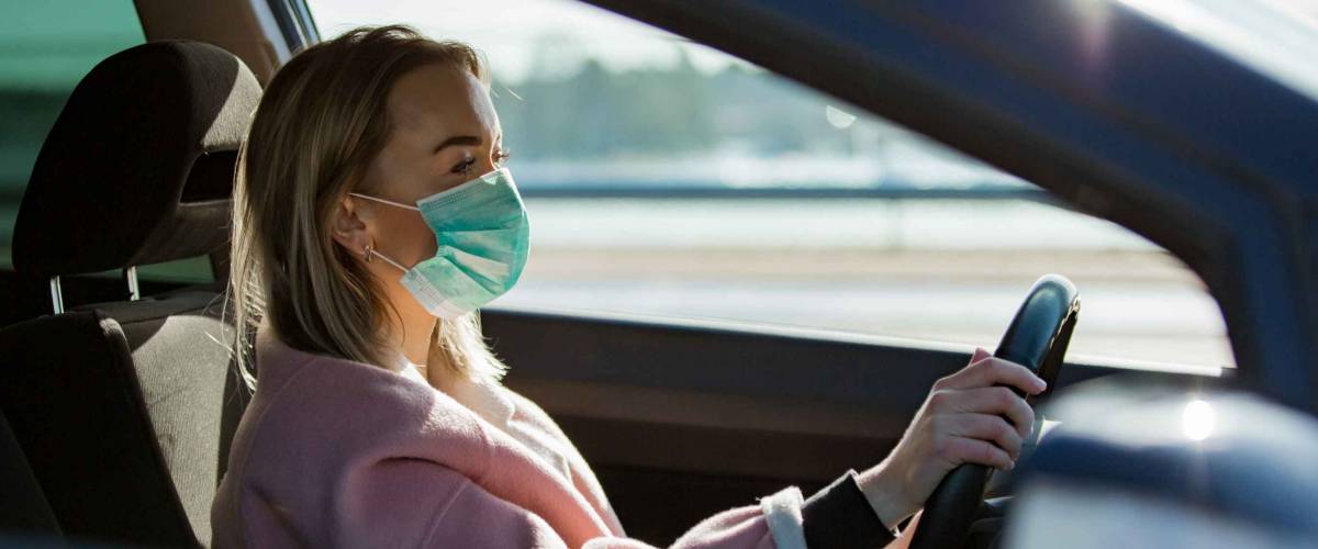 Woman in protective mask driving a car on road.
