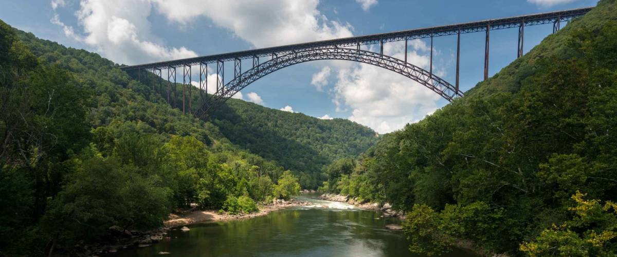 Rafters float towards the rapids under the high arched New River Gorge bridge in West Virginia