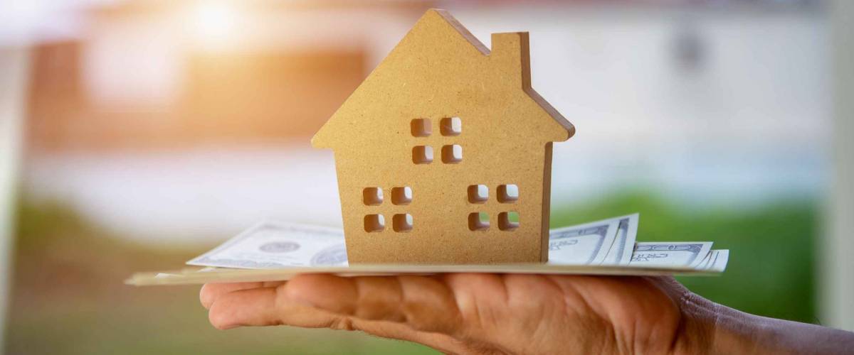 A model house on top of cash, symbolizing mortgage closing costs