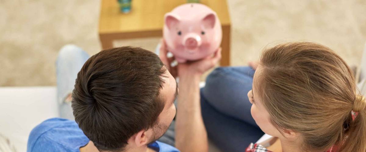 money, home, finance and relationships concept - close up of couple with piggy bank sitting on sofa