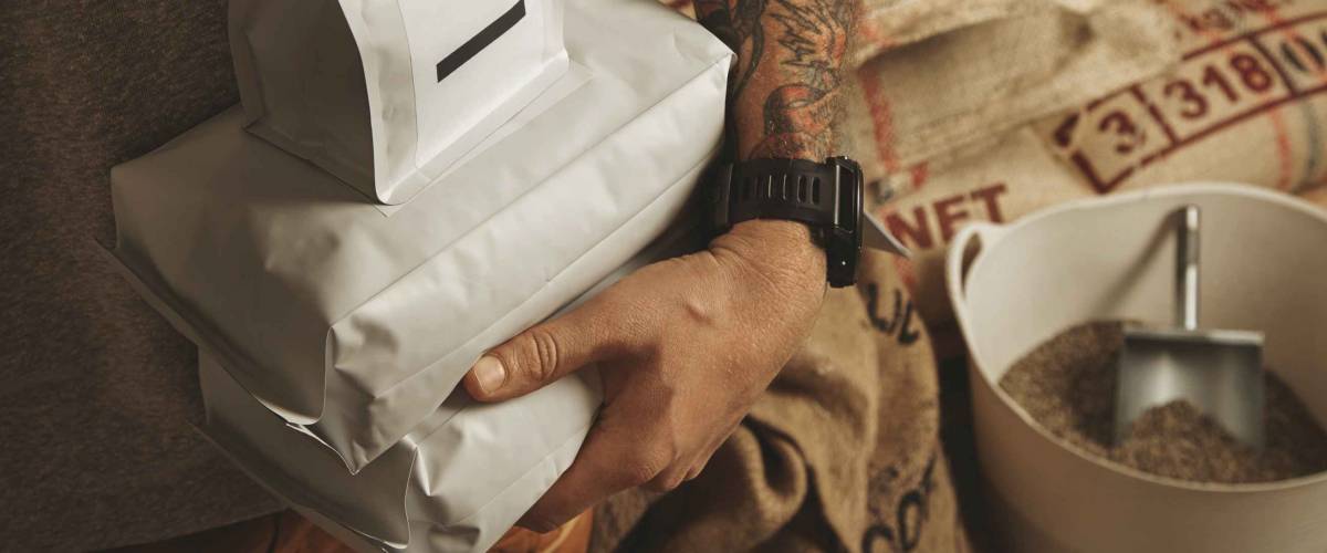 Tattooed barista holds bags with freshly bake coffee beans ready for sale and delivery
