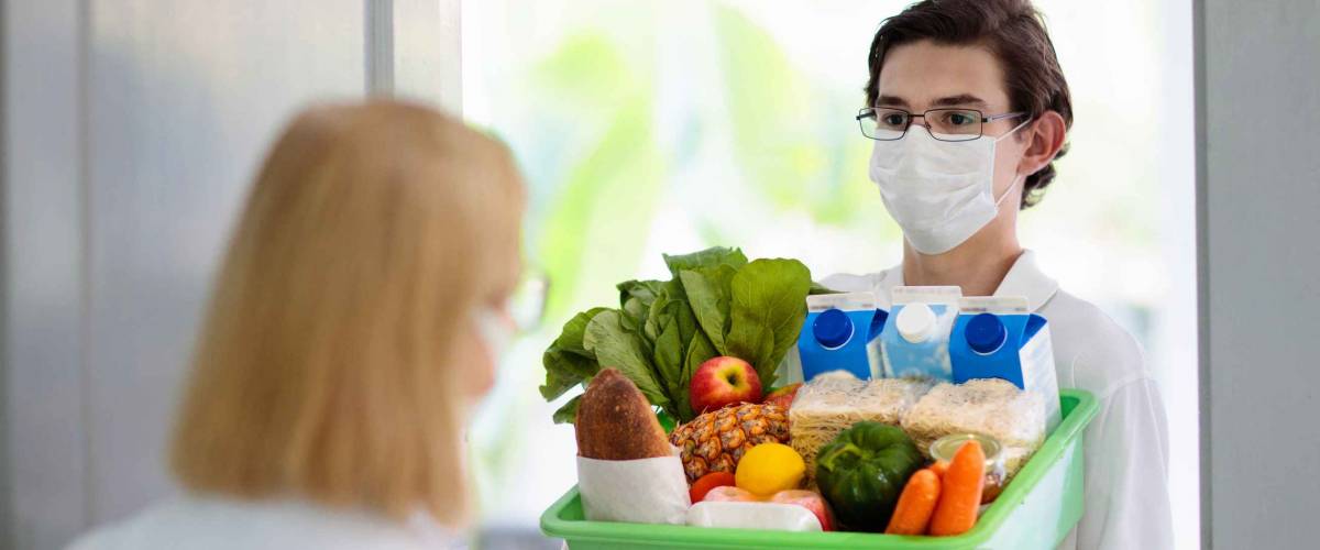 Food delivery during corona virus outbreak. Courier wearing face mask delivering grocery order in coronavirus epidemic. Safe shopping in pandemic. Takeout meal. People stockpile food.