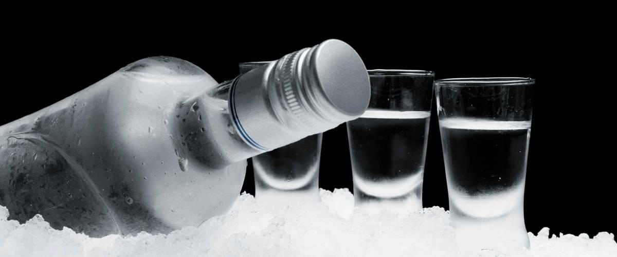 Close-up view of bottle of vodka with glasses standing on ice on black