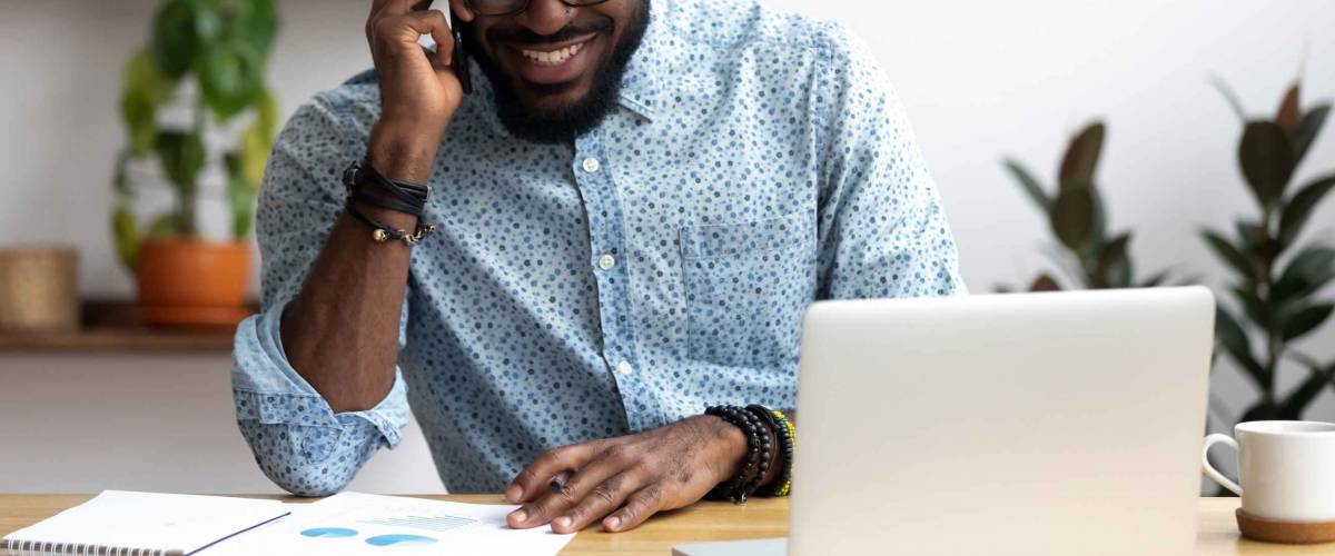 Man sitting at office desk in front of laptop holding phone