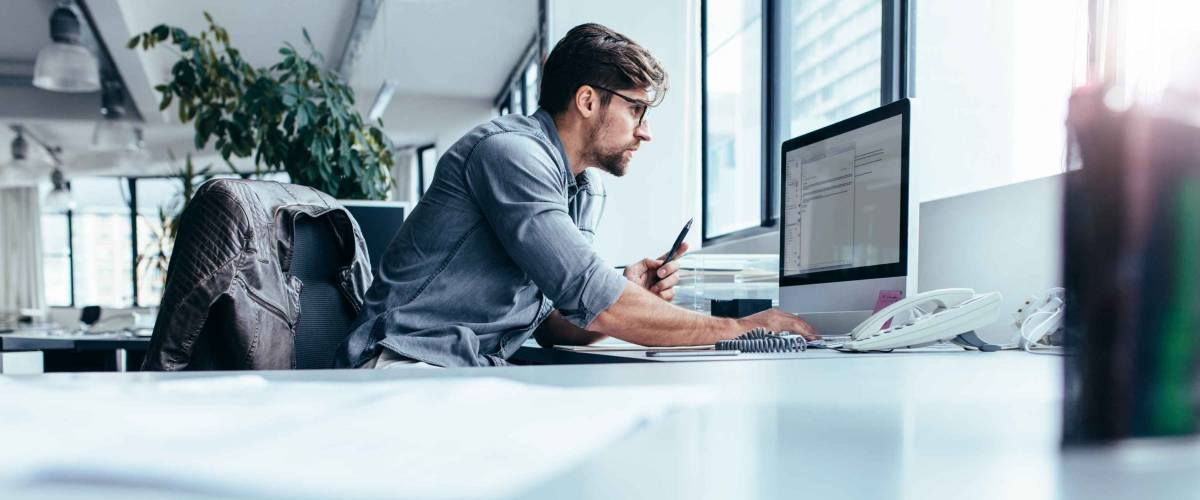 Young man sitting in office and working on desktop pc. Businessman looking at computer monitor while working in office.