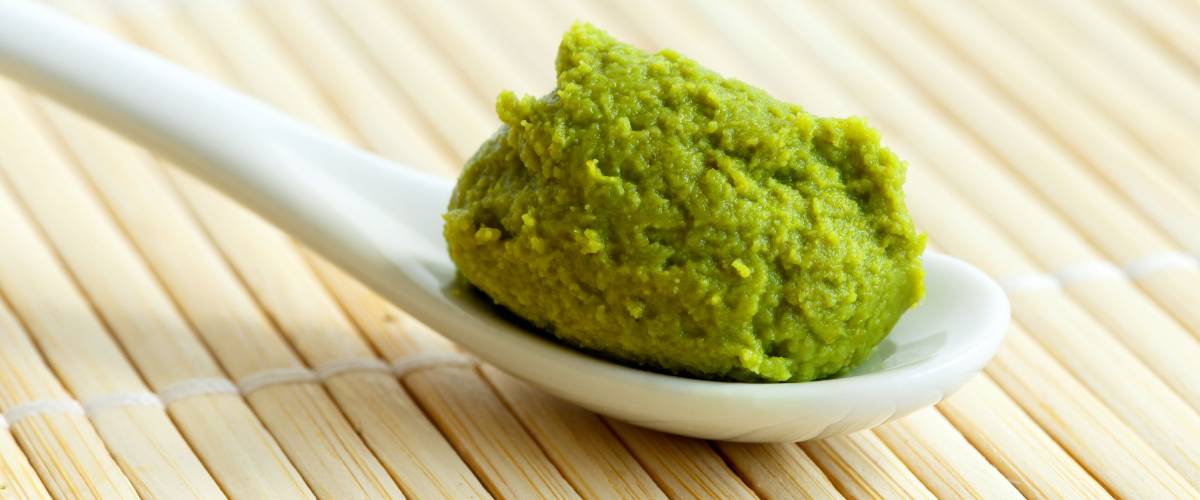Wasabi paste on ceramic spoon on bamboo mat.
