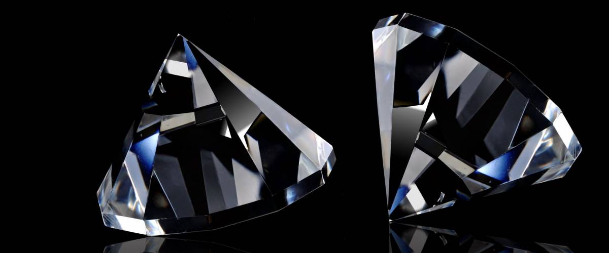 Two loose diamonds on black reflective surface