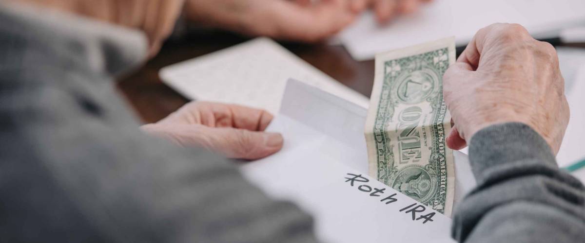 cropped view of man holding envelope with 'roth ira' lettering and dollar banknote