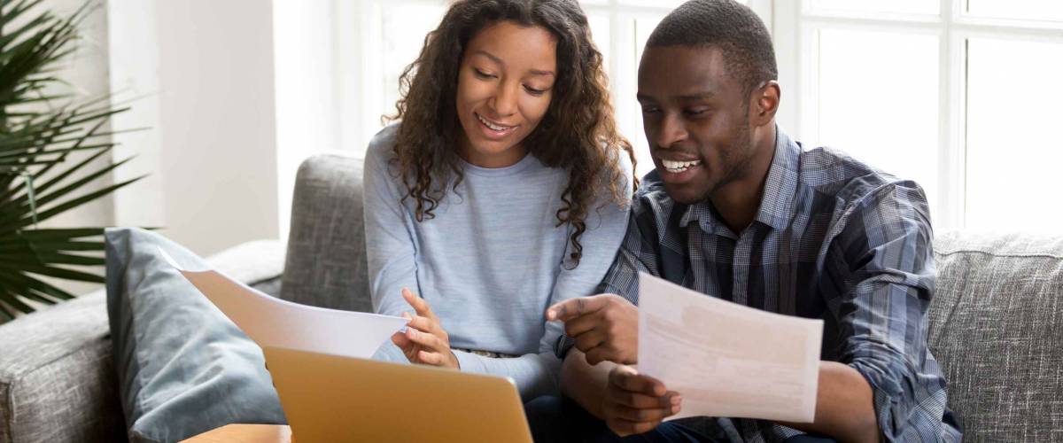 Black married couple sitting on sofa at home reading documents