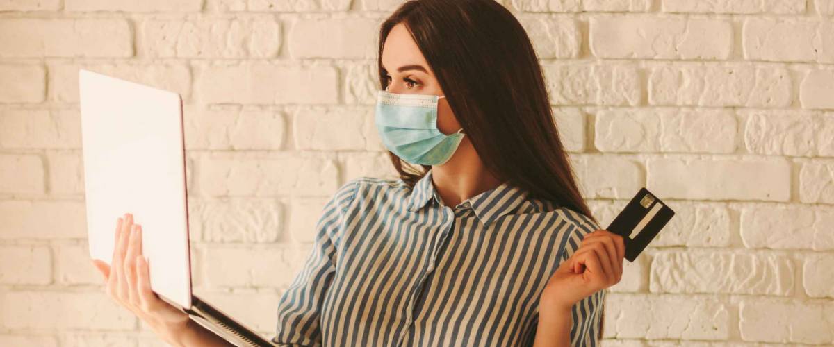 Shopper in protective face mask hold laptop, credit card and shopping bag
