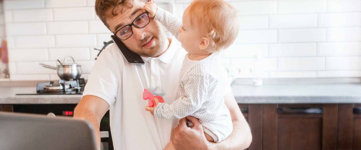 Handsome young man working at home with a laptop with a baby on his hands. Stay home concept. Home office with kids.