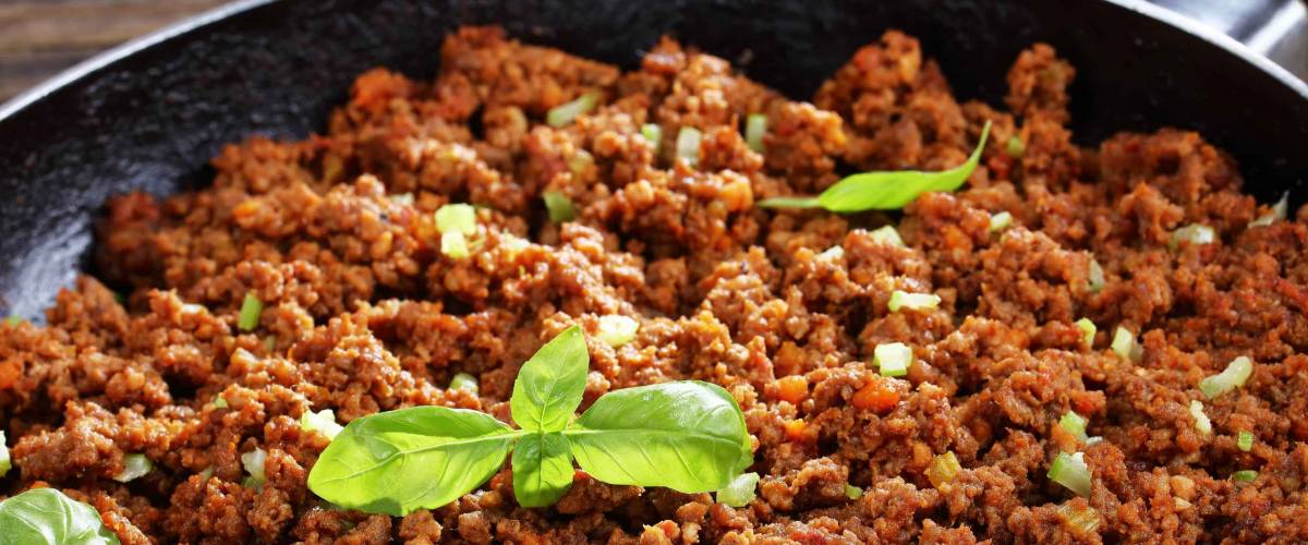 close-up of hot juicy ground beef stewed with tomato sauce, spices, basil, finely chopped vegetables and celery in frying pan, classic recipe, side view from above
