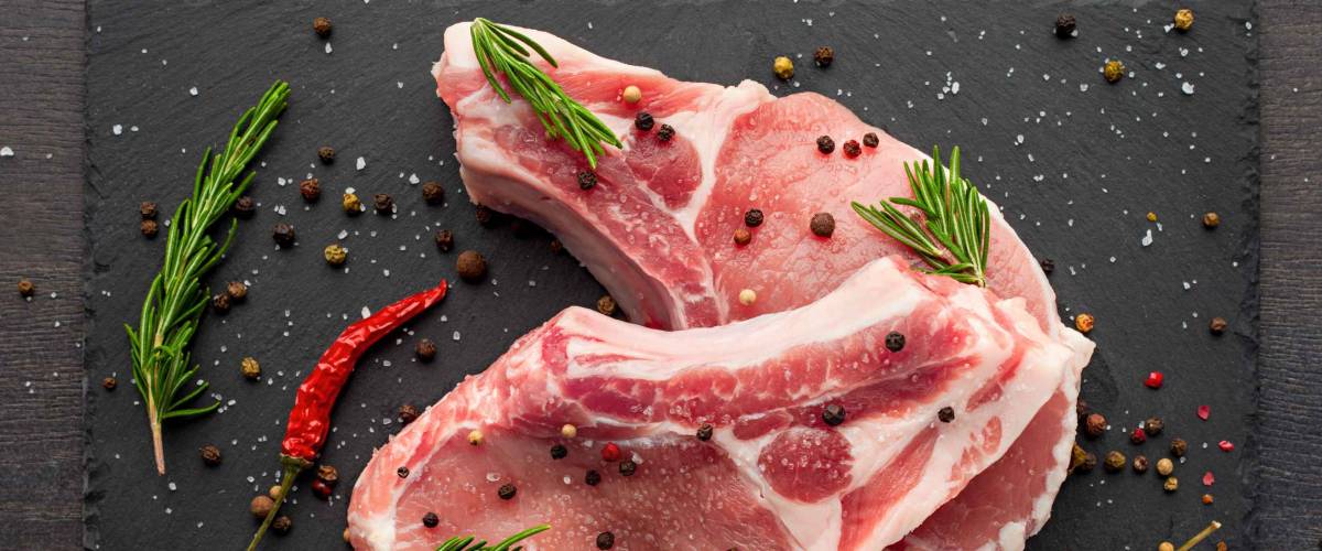 fresh raw meat with spices and rosemary and red pepper on black slate, on dark background, pork, beef, chop on a bone