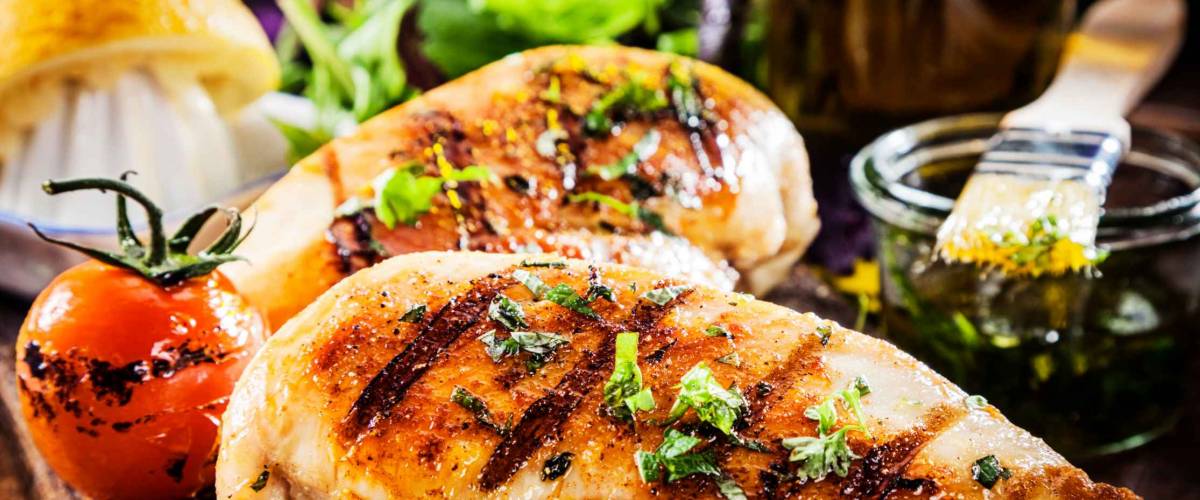 Marinated grilled healthy chicken breasts cooked on a summer BBQ and served with fresh herbs and lemon juice on a wooden board, close up view