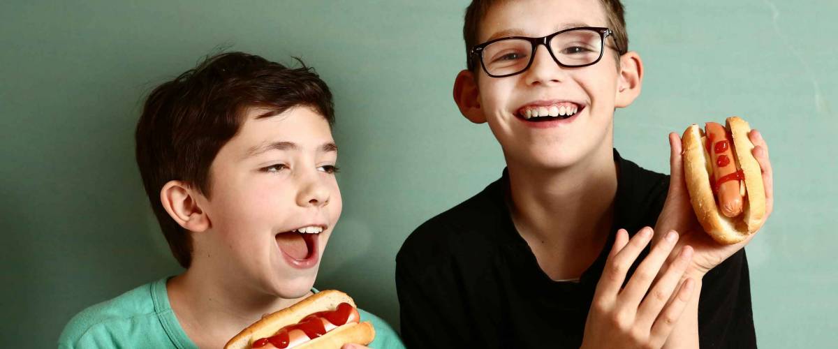 teenager school boys cooking eat hot dog happy smiling laughing closeup portrait on blue wall background