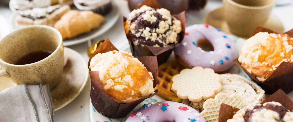 Fresh donuts, cookies and muffins on served table with cups of tea near by