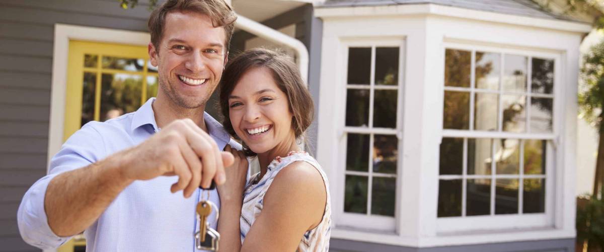 Couple With Keys Standing Outside New Home