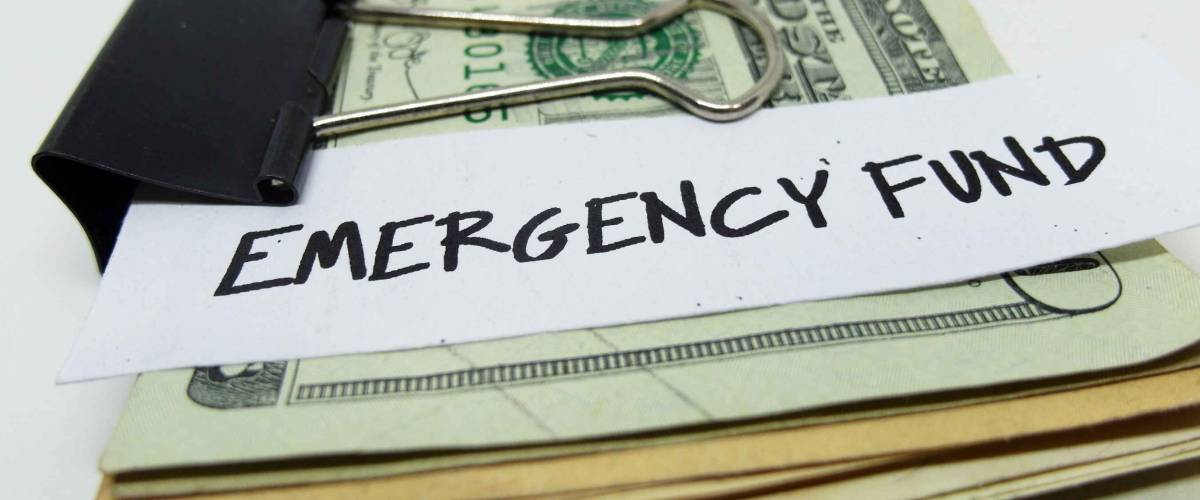 Closeup of US dollars in paper clip on white background with note written EMERGENCY FUND : Concept of setting money saving goal for rainy day.