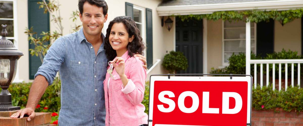 Hispanic couple outside home with sold sign