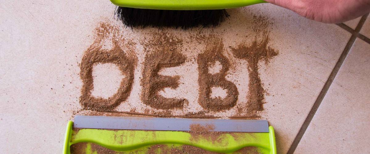 Sweep debt clean concept with debt written in dirt on a floor and a person is about to sweep the debt dirt in a dust pan using a small hand broom