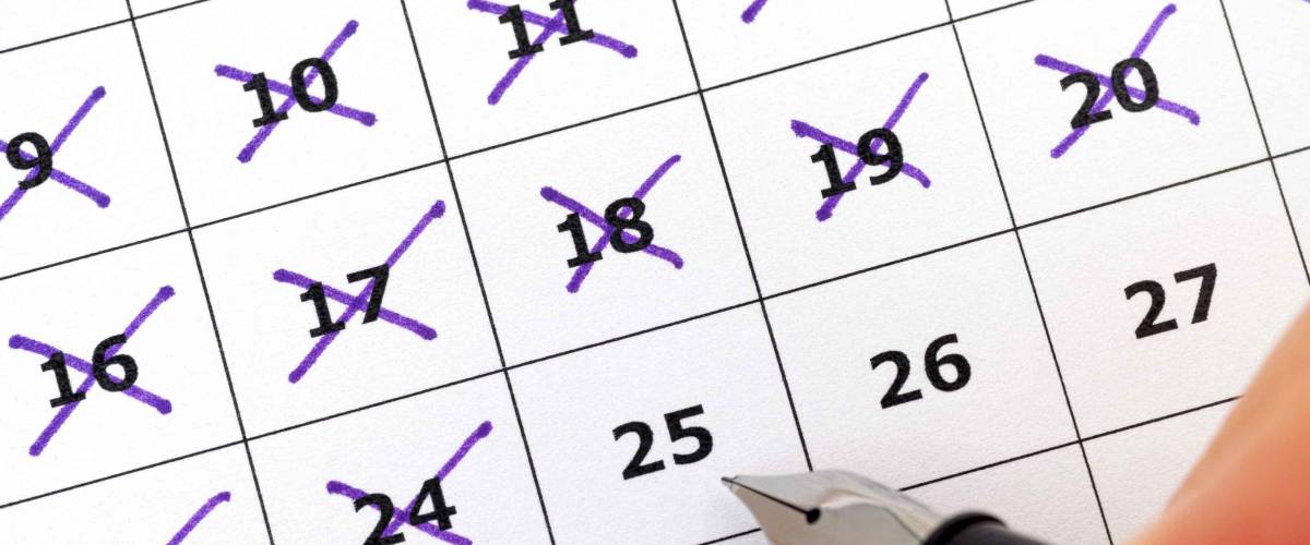 Fountain pen in human hand marking days on calendar. Focus on calendar.