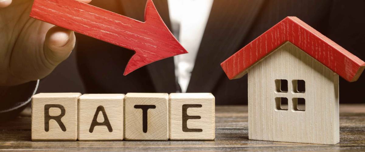 Businessman holding the down arrow on wooden blocks with the word Rate and house. Low interest in mortgages. Reducing interest payments for mortgage. The fall in housing rates on credit.