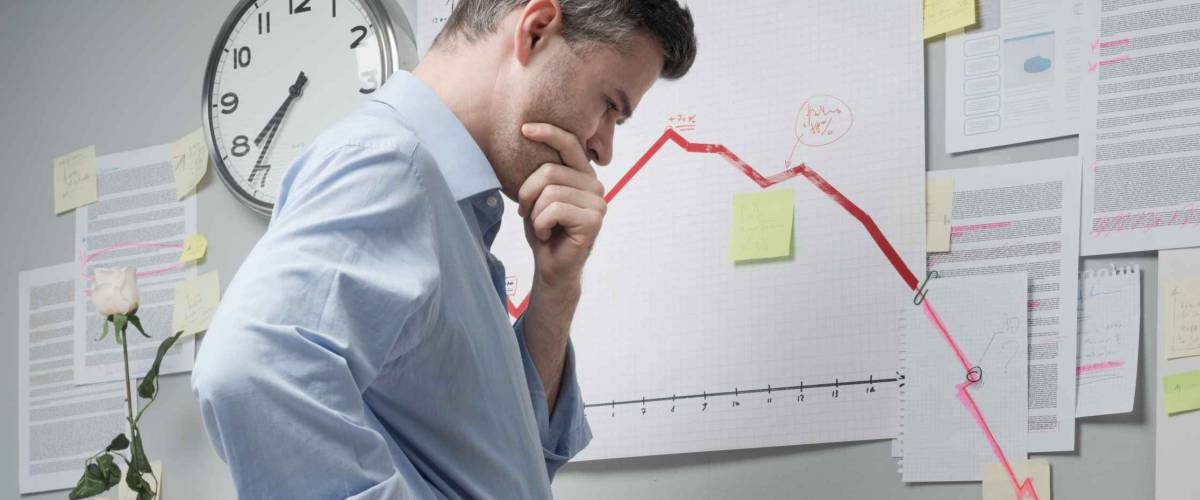Concerned businessman at work looking at negative business chart with arrow going downwards.
