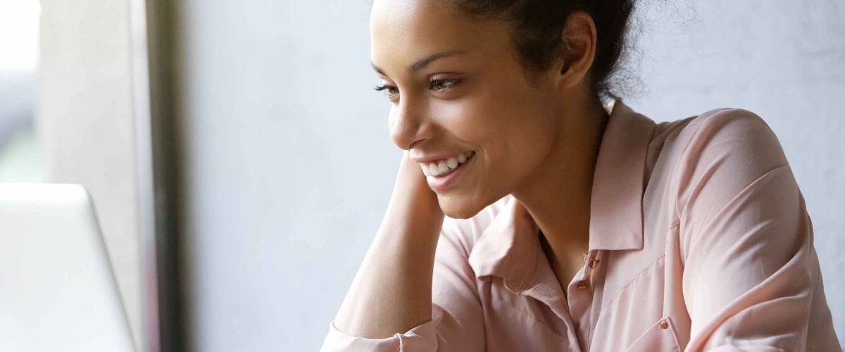 Close up portrait of a beautiful young woman smiling and looking at laptop screen