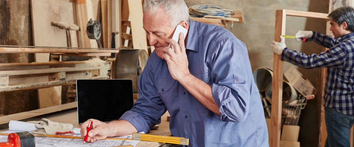 Senior as executive chief with smartphone at carpentry shop