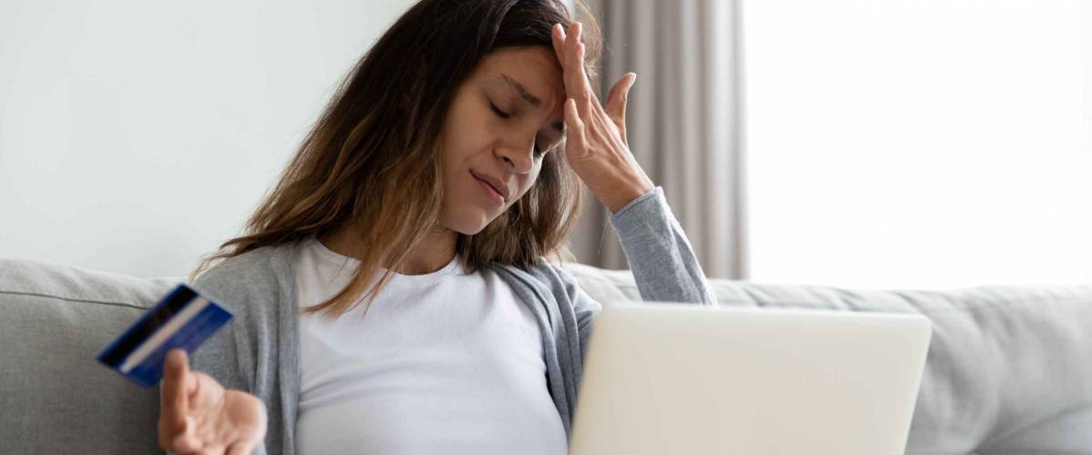Millennial woman sit on sofa feels stressed using laptop holding plastic credit card because she's been scammed.