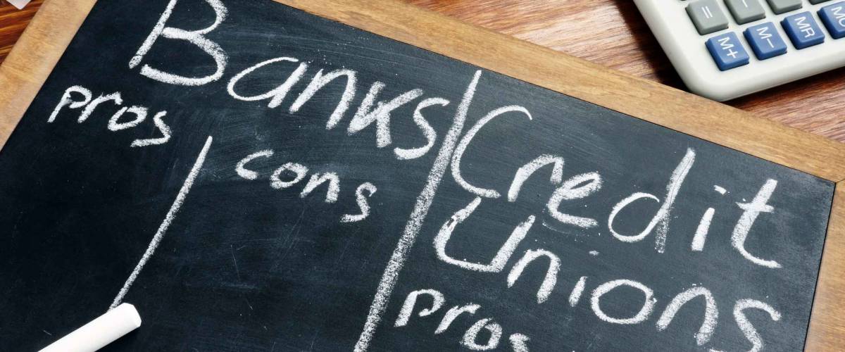 Banks vs. Credit Unions pros and cons written on a blackboard.