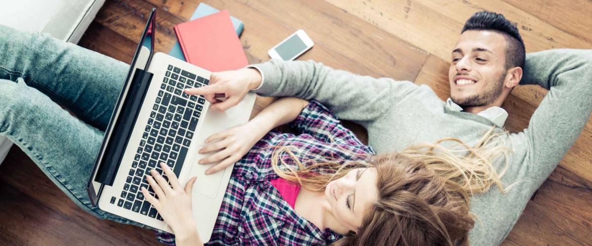 Couple shopping online at laptop computer - Two young friends watching a video on a notebook in the living room, view from above