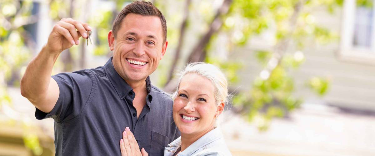 Caucasian Couple in Front of House with Keys.