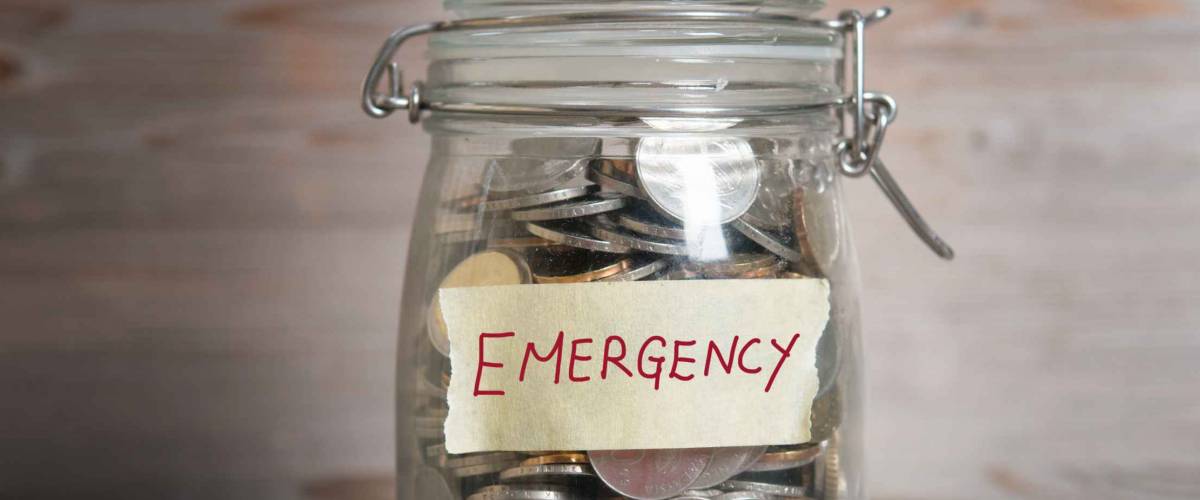 Coins in glass money jar with emergency label, financial concept. Vintage wooden background with dramatic light.