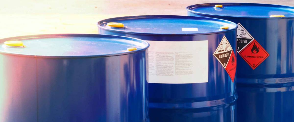 the close-up shot of blue color hazardous dangerous chemical drum barrels ,have warning labels of corrosive & flammable liquid in daylight on daytime.