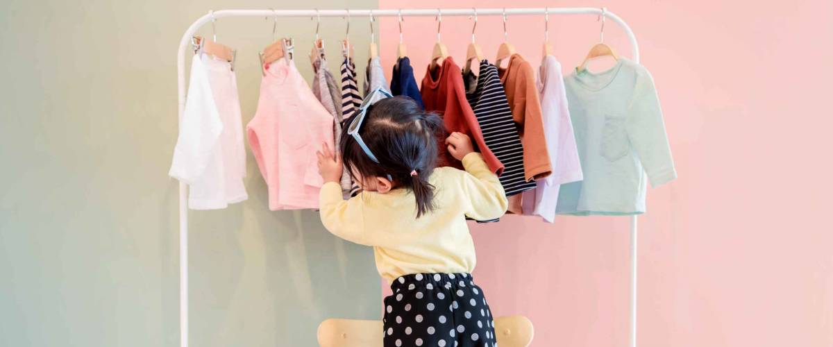 Soft Focus of a Two Years Old Child Choosing her own Dresses from Kids Cloth Rack