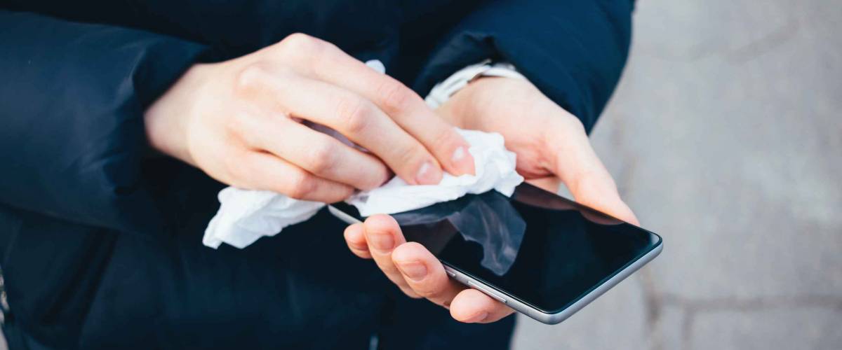 Woman's hands wipe smartphone screen with disinfectant cloth.