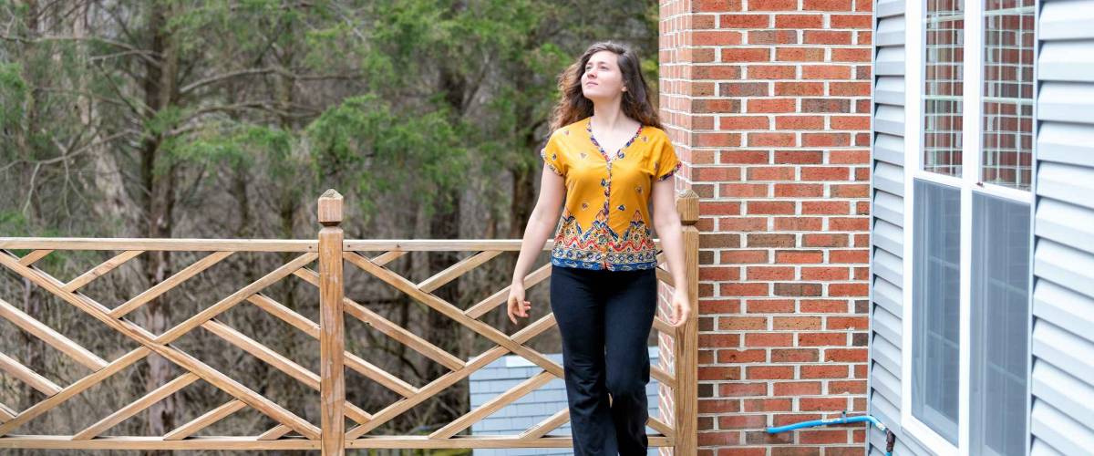 One young woman walking outside, outdoors barefoot on wooden house, home deck, looking up, homeowner at backyard, front yard