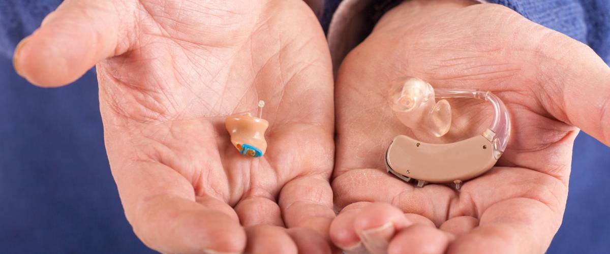 Old man's hand showing a CIC (completely in canal) and a BTE (behind the ear) hearing aids