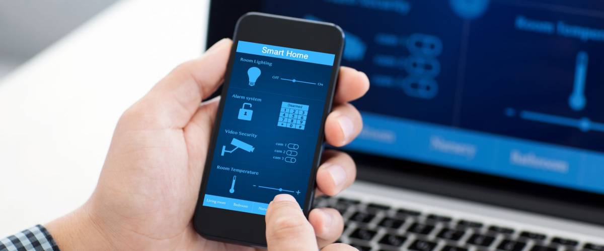 man holding the phone with program smart home on the screen against the background of the computer