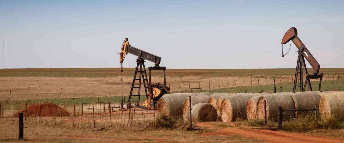 A scene from rural Oklahoma. Oil pumps and hay bales in the prairie.