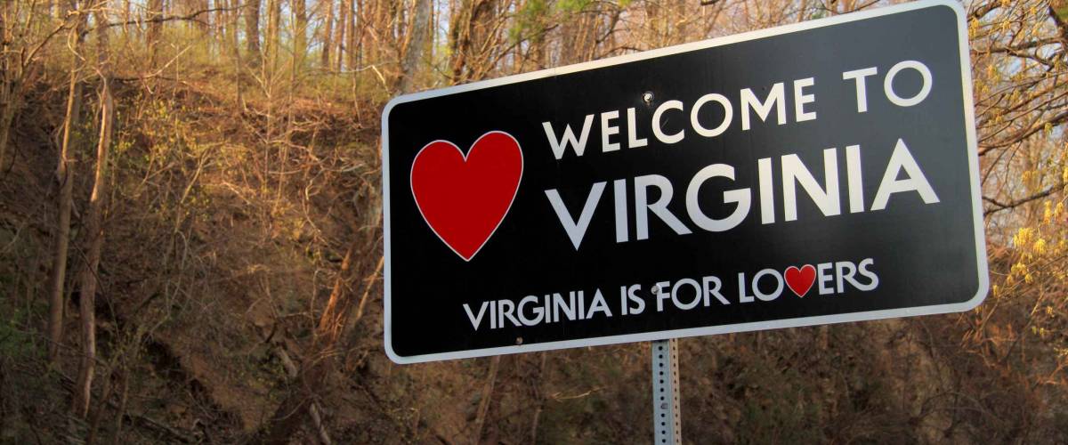 A roadside sign welcomes travelers along a rural road to the state of Virginia