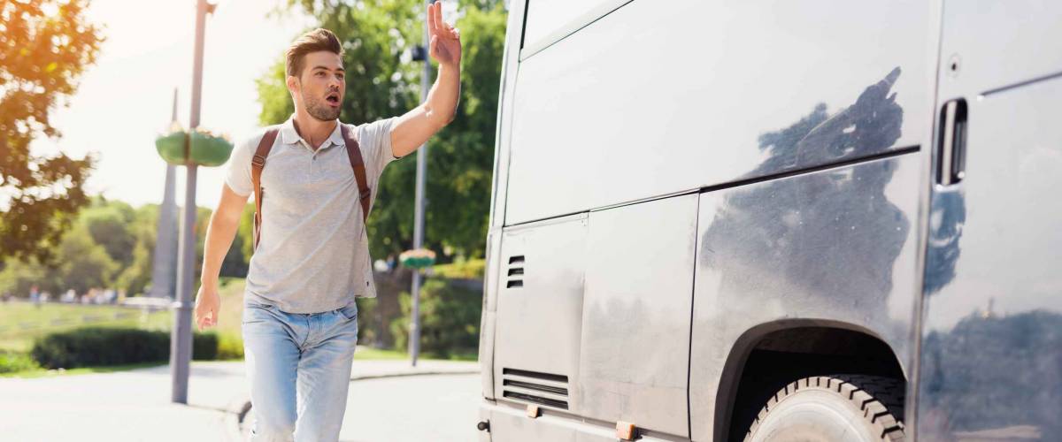 The guy runs after the bus that leaves. He missed the bus and tries to catch up with him. He runs after a modern black bus and waves his hand to stop it.