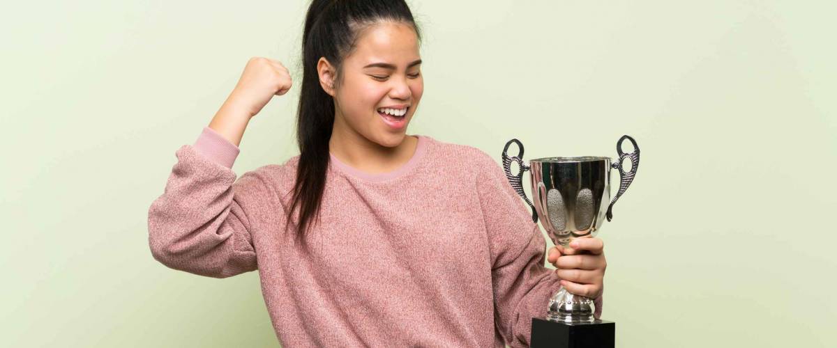 Young teenager Asian girl over isolated green background holding a trophy