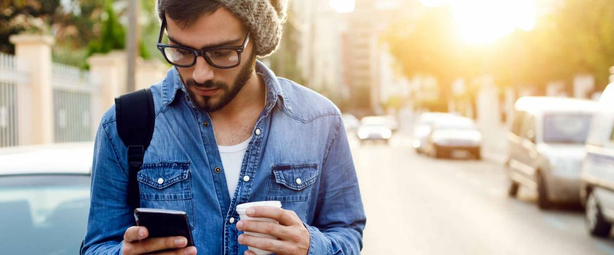 Outdoor portrait of modern young man with mobile phone in the street.