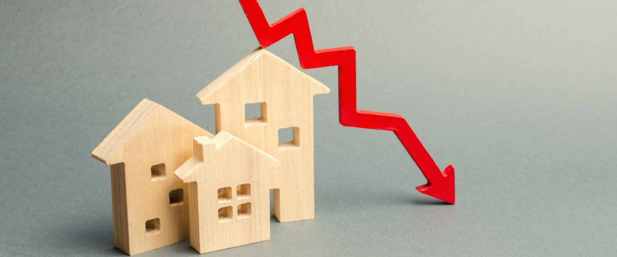 Miniature wooden houses and a red arrow down. The concept of falling mortgage rates.