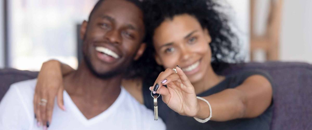 Excited young Black couple show keys to new home.