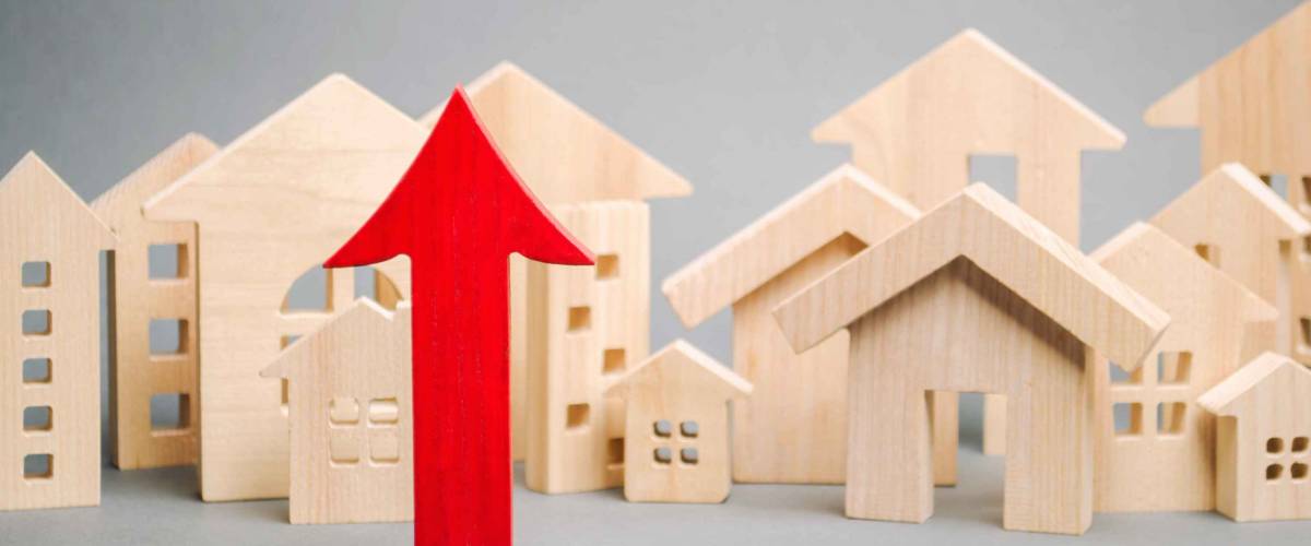 Red arrow up and miniature wooden houses. The concept of rising property prices.