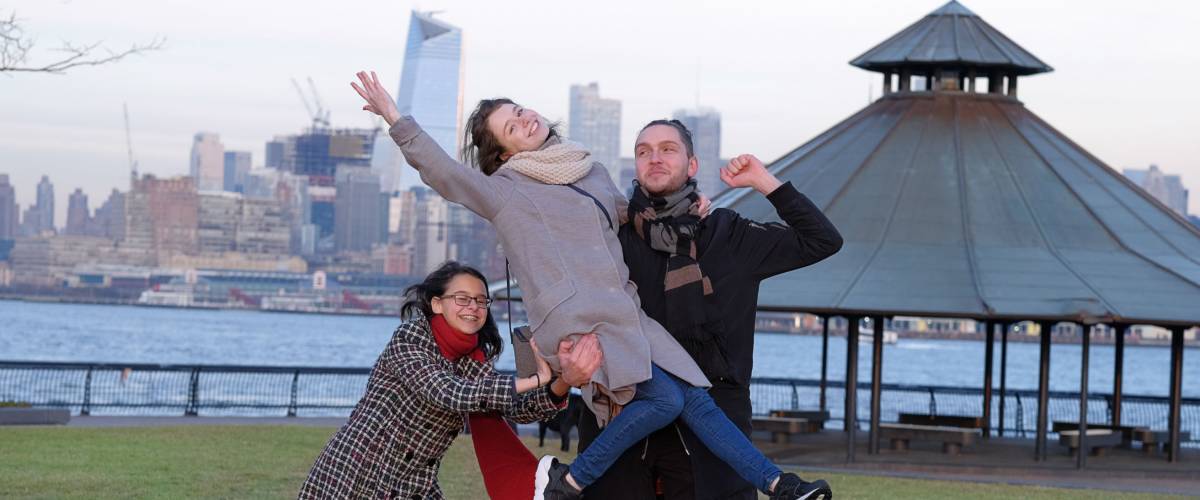Group of young people walking in cold day, having fun/ Downtown of Manhattan on the background/Young people grimace, show language.